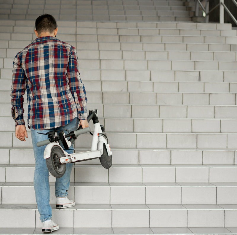 homme jean montant escalier trotinnette main