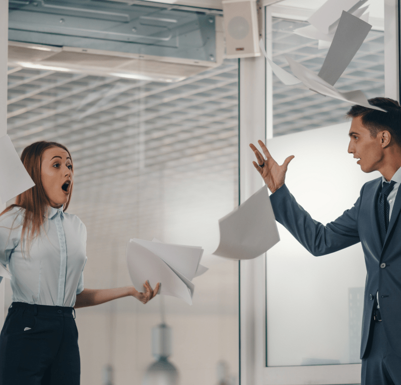 Homme qui jette des feuilles de papiers dans une bureau face à une employée - header les soft skills incontournables du manager