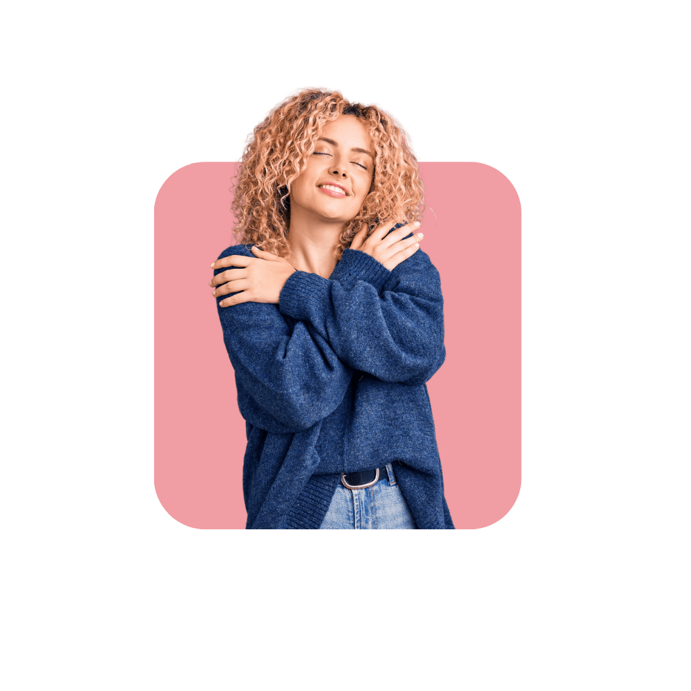 Femme avec un pull bleu et un jean se faisant un câlin sur fond rose.